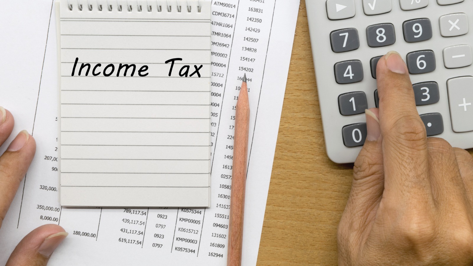 Person using a calculator with a finger and a pencil lying in between the calculator and a paper which has Income Tax Labeled